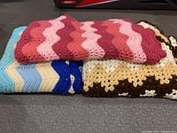 Three folded crochet blankets stacked together showing different patterns and colors