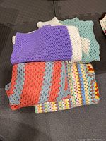Four crochet blankets stacked showing variety of colors and patterns