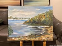 Full view of the landscape painting showing water, trees with autumn colors, sky, and distant hills, signed by E Lambert.