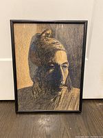 Full front view of framed art piece showing the portrait of a person in sepia and black tones, framed in a black frame, standing upright.