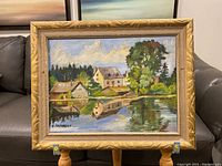 Full view of the framed oil painting depicting houses and water reflection.