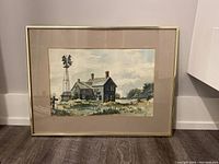 Full view of the framed watercolor painting showing the rural house, windmill, and fence under cloudy sky.