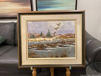Full view of the framed Minns painting showing a winter landscape with a river and flying ducks.