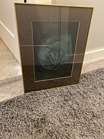 Framed vintage art print shown standing on floor near baseboard, showcasing the overall piece with gold frame and matting.