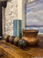 Photo showing the tall striped ceramic vase, four decorative balls of different finishes, and the medium copper pot on wooden surface.