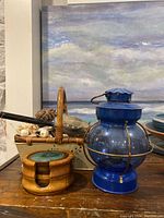 Photo of a blue metal and glass vintage lantern, wooden basket with pinecones and garlic, and round wooden coasters with turquoise stone inlay on a wooden table.