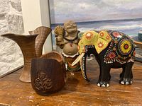 Wooden coasters with floral carvings in holder, painted elephant figurine, Laughing Buddha statue on wooden surface