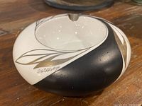 Photo of the round ceramic ashtray showing the black, white, and gold leaf design with the signature 'J. Wilberg'.