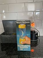 Photo of boxed Waterful Needle Nose game, marbles, and working flower lamp in background