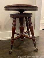 Full view of Victorian wooden piano stool showing round seat, turned legs, stretchers, and claw feet with glass balls.