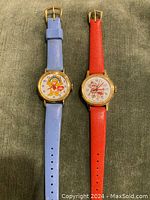 Pair of wristwatches placed side-by-side showing full straps and dial characters: blue strap with Care Bear and red strap with Strawberry Shortcake.