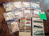 Nine clear zip bags filled with vintage Victorian diecuts laid out on a wooden table alongside a complete vintage scrapbook showing ships and cars.