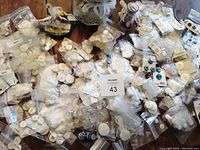 Photo showing numerous small bags with assorted white and cream buttons, many still on original cards, spread out on a surface.