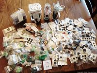 Wide view of the table displaying a large quantity of vintage buttons, many in plastic bags, some on cards, and multiple vintage containers in the background.