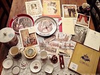 Overview of large array of vintage Queen Elizabeth II memorabilia including books, portraits, trays, tins, postcards, dishware, and printed cards on a table.