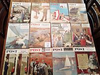 Photo showing 12 Saturday Evening Post magazines laid out on a table, displaying their illustrated covers with various scenes including outdoor activities and formal meetings.