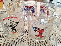 Four clear mugs including two Disney collectible mugs with Steamboat Willie and Fantasia Mickey Mouse, and two others with USA patriotic designs.