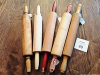 Five wooden rolling pins laid flat on wooden surface, showing full length including handles; includes two pins with red painted handles and three with natural wood handles.