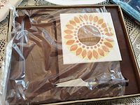 Boxed 1960s wooden cheese tray with sunflower ceramic inlay, partially visible inside plastic wrapping