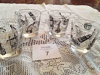 Four vintage mid-century modern hi ball glasses arranged on a lace tablecloth showing black musical instrument designs such as guitar, drums, and violin motifs.