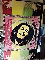 Full front view of the large woven Bob Marley fabric wall hanging showing the colorful sectioned background, central portrait, geometric border, and lion silhouettes.