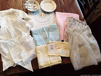 Overview photo of entire lot showing linens, knitted blankets, white clothing, and Portuguese children's china dishes with cutlery.