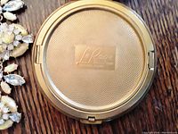 Close-up photo of the back of the vintage Le Rage gold-tone compact showing textured pattern and brand name.