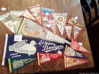View of all 17 vintage pennants laid out on table showing variety of designs including Los Angeles Dodgers stadium, Bermuda, San Francisco, and other travel locations.