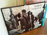 Framed black and white poster of a romantic street scene with a couple kissing and blurred pedestrians around, by Robert Doisneau.