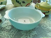Light blue Pyrex mixing bowl with handles shown on lace tablecloth