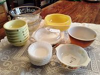 Overview of various mixing bowls, casseroles, and dessert bowls including sunny yellow, clear glass, and white ceramic items with fruit motifs on some casseroles.