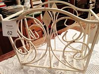 Front and side angle view showing the ornate wrought iron scrollwork and diamond accents on the painted white mid-century magazine rack.