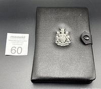 Closed black leather coin case with silver emblem and snap closure