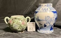 Front view of two decorative vases/planters, one blue and white with Asian landscape, the other green with floral and bird design and handles.