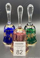 Three colorful crystal bells in blue, red, and green with clear crystal handles and gold floral gilt decoration.