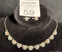 Set of silver necklace and matching turquoise earrings displayed on a black stand showing details of floral turquoise accents on the necklace and the small matching earrings
