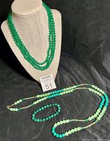 Full lot view showing three-strand jade necklace, long jadeite and malachite necklace, and stretchy malachite bracelet on black background