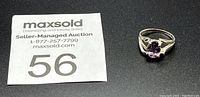 Photo of the sterling silver ring with an oval amethyst stone alongside auction lot number 56 tag on a black background.