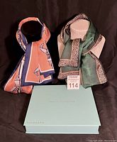 Two scarves with Tiffany & Co. blue box below them, shown on black background, scarves display distinct colors and patterns