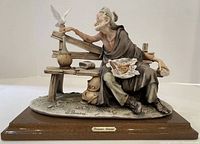 Full front view of the sculpture showing an elderly man sitting on a bench and feeding a dove, signed by Giuseppe Armani and mounted on a wooden base with nameplate.