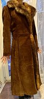 Front view of brown suede coat with fur collar and fur lining along front edges, showing long fitted sleeves and waist seam.