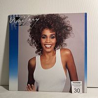 Front cover of Whitney Houston self-titled LP showing the artist smiling with curly hair and wearing a white tank top.