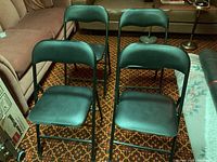 Four black folding chairs arranged in two rows, showing padded seats and backs with black metal frames.