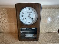 Front view of Brentwood 31 Day clock in wooden case showing clock face, lower day-date display and glass covering.