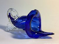 Side view of cobalt blue and clear glass cornucopia vase with twisted clear handle and flared opening.