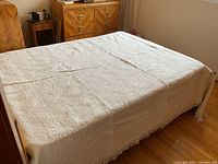 Full view of white bedspread on bed showing overall size and fringe on three sides.