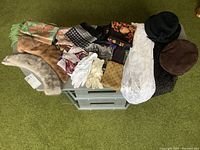 Top-down view of all items on a small green table showing fur collars, hats, scarves, gloves, and shawls arranged side by side.