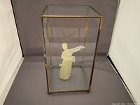 Full view of the closed glass showcase with brass frame containing the green figurine.