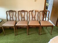 Four walnut framed dining chairs with curved decorative backs and patterned upholstered seats arranged side by side on green carpet.