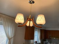 Photo of the three-light ceiling fixture mounted and illuminated showing the etched floral pattern on the frosted glass shades and wooden arms.